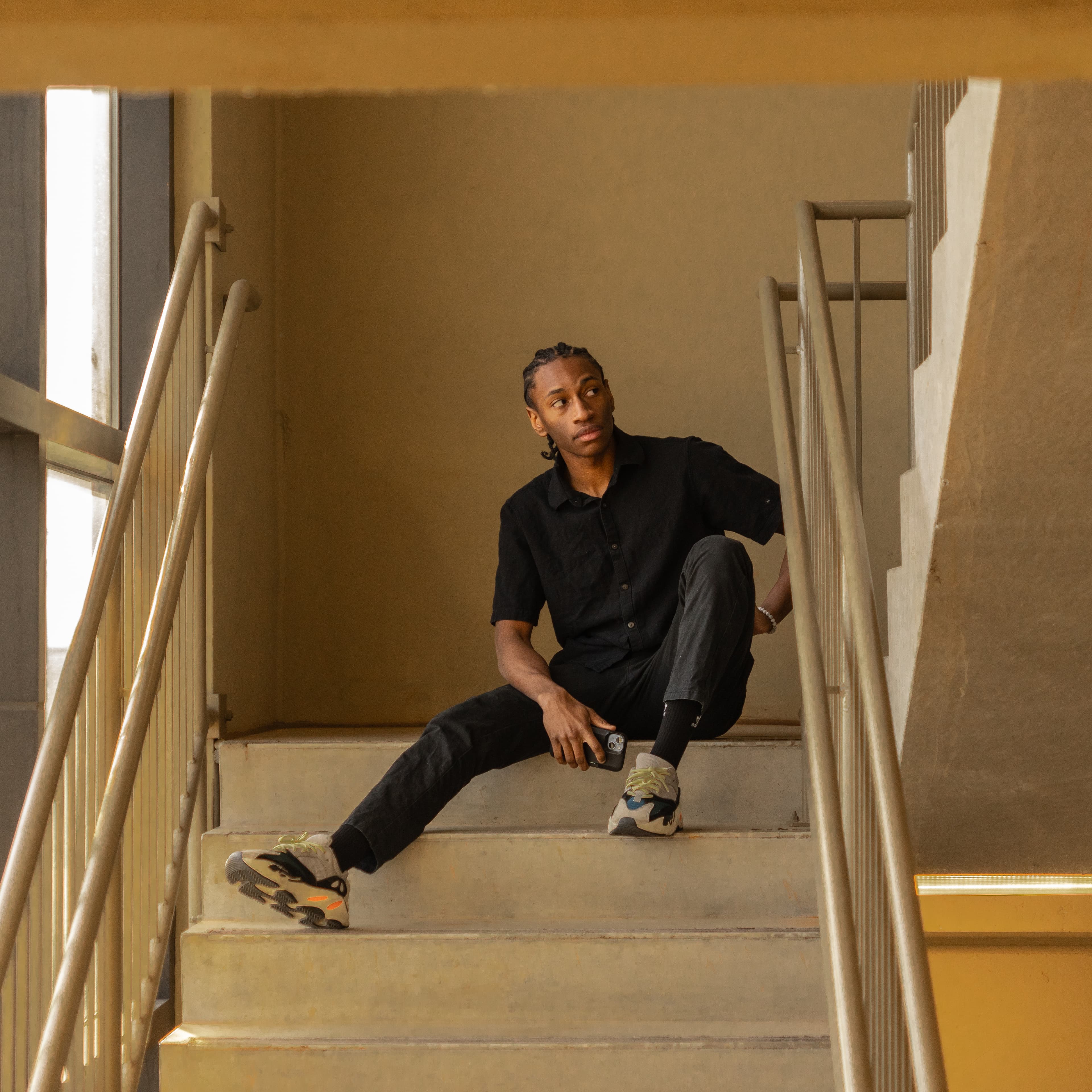 Tyshawn Allison — all black outfit, seated on staircase, warm tones